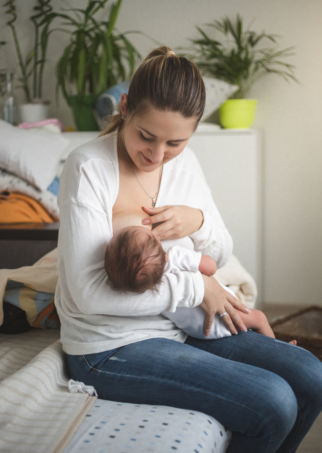 Beautiful young mother breastfeeding little baby in living room